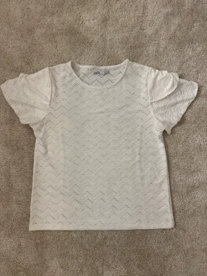 Söt vit topp  - Säljer en vit blus från Isolde med vågigt broderat mönster och korta ärmar. Perfekt för dig som gillar stilrena toppar med lite extra detaljer.