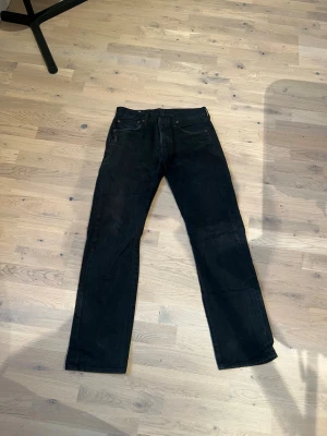 Svarta raka jeans från Levi's 501 - Säljer ett par svarta jeans från Levi's med klassisk rak passform och fem fickor. Jeansen har en diskret läderpatch bak i midjan och är tillverkade i slitstark denim. Perfekta till en avslappnad streetwear-look. Storlek W 31 L 32