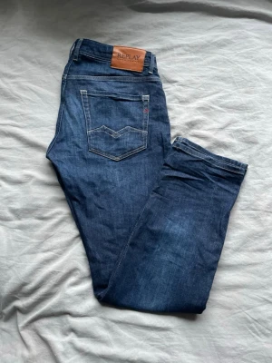 Mörkblå jeans från Replay - Snygga mörkblå jeans från Replay med klassisk femficksdesign och läderpatch bak i midjan. Jeansen har raka ben och tydliga sömmar, tillverkade i denim med en cool tvättad look. Perfekta för en avslappnad och trendig stil.