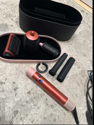 Dyson Airwrap hårstyler set röd/rosa - Säljer ett Dyson Airwrap hårstyler set i röd och rosa med flera tillbehör: rundborste, borsthuvud, locktillbehör och förvaringsbox. Perfekt för att styla och forma håret med olika effekter. Snygg och modern design.