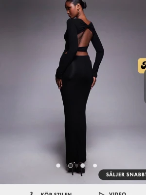 Svart långklänning med öppen rygg - Elegant svart långklänning med långärmad design och snygg öppen rygg. Klänningen har en figurnära passform och stilren siluett som framhäver formerna. Perfekt för dig som vill ha en modern och trendig look.