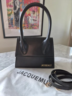 Svart Jacquemus Le Chiquito handväska - Snygg svart handväska från Jacquemus i modellen Le Chiquito. Väskan är tillverkad i slätt läder med guldfärgad logga framtill och har ett avtagbart axelband. Stilren och kompakt design med två handtag och magnetlås. Sample väska 