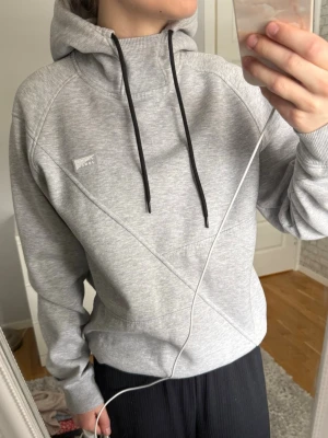 Grå hoodie från Jack & Jones - Snygg ljusgrå hoodie från Jack & Jones med svart dragsko i huvan och diskret logga på bröstet. Hoodien har ribbade muddar. Perfekt till chill dagar och enkel att matcha med det mesta.