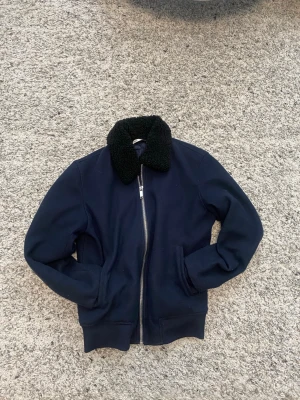 Mörkblå bomberjacka med teddykrage - Snygg mörkblå bomberjacka med dragkedja framtill och svart teddykrage. Jackan har ribbade muddar vid ärmslut och nederkant samt två fickor på sidorna. Perfekt för dig som vill ha en stilren och trendig look.     Pris kan diskuteras 😁
