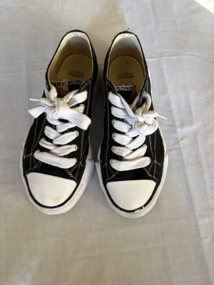 Svarta låga sneakers med vita detaljer - Svarta sneakers från Jimmy med vit tå, vita skosnören och vit sula. Klassisk låg modell med tydliga kontrastsömmar och canvasmaterial. Perfekta för en avslappnad och stilren look.