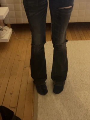 Svarta bootcut jeans Gina Tricot - Säljer ett par svarta bootcut jeans från Gina Tricot med slitningar vid knäna och råa kanter. Jeansen har en klassisk femficksmodell och är tillverkade i ett stretchigt denimtyg som sitter snyggt på benen.