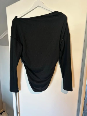 Svart långärmad topp med sned axel - Stilren svart långärmad topp med sned axel och draperad effekt i midjan. Tunn och mjuk kvalitet, perfekt att styla med jeans eller kjol. Aldrig använd