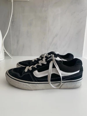 Svarta Vans Old Skool sneakers - Säljer ett par klassiska Vans Old Skool sneakers i svart med vit sidostrip och vita snören. Skorna har låg profil och är tillverkade i canvas och mocka med gummisula. Perfekta för dig som gillar streetstyle och skatekultur. Lappen ska vi limma på om någon köper!