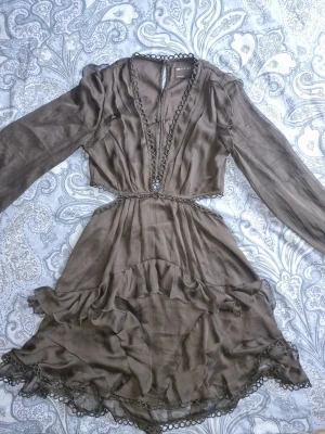 Svart omlottklänning med volang - Supersnygg svart kortklänning från Asos med omlott-look, volangdetaljer och spets längs kanterna. V-ringning och cut out detaljer vid midjan. Perfekt för dig som gillar unika detaljer och flowy material. Använd ca 3 gånger.