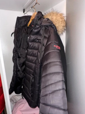 Svart dunjacka med fuskpäls från Navahoo - Snygg svart dunjacka från Navahoo med quiltad design . Jackan har dragkedjor på fickorna och detaljer på ärmen. Perfekt för våren och ger en modern look.jag har sytt om den så den är figursydd och tight i midjan 
