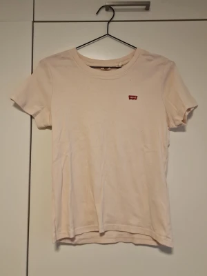 Ljusrosa t-shirt från Levi's - En enkel och stilren ljusrosa t-shirt från Levi's med klassisk rund halsringning och korta ärmar. Liten röd Levi's-logga på bröstet. Tillverkad i mjuk bomull för en bekväm känsla.