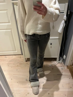 Grå bootcut jeans med slitningar - Säljer ett par grå bootcut jeans med lätt slitna detaljer och klassisk femficksmodell. Jeansen har en snygg tvättad look och sitter tajt över låren för att sedan bli vidare nedtill. Perfekta för dig som gillar en avslappnad men trendig stil.
