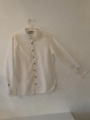 Vit slim fit skjorta från Mango Man - Klassisk vit skjorta från Mango Man i slim fit-modell. Skjortan har långa ärmar, svarta knappar och en stilren design 