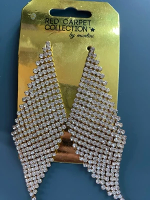 Glittriga örhängen från Montini - Säljer ett par statement örhängen från Montini Red Carpet Collection. Örhängena är silvriga med massor av gnistrande stenar i ett elegant, triangelformat mönster. Perfekta för dig som vill sticka ut och addera extra glamour till din look.