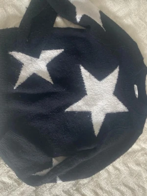 Svart stickad tröja med vita stjärnor - Cool svart stickad tröja med stora vita stjärnor på både fram- och baksida. Tröjan har en avslappnad passform och långa ärmar. Perfekt för dig som gillar statement-plagg och vill sticka ut lite extra.