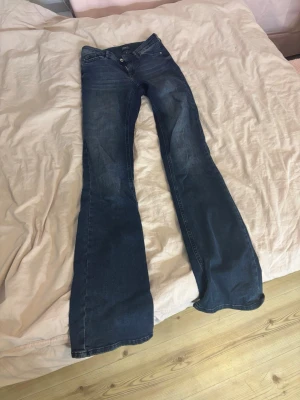 Mörkblå bootcut jeans - Säljer ett par mörkblå bootcut jeans med mid waist och klassiska fem fickor. Jeansen har en lätt tvättad look och vida ben som ger en retrovibe. Perfekta för dig som gillar en avslappnad men ändå trendig stil.