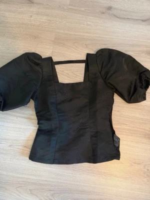 Topp  - Superfin och feminin topp i klassisk svart färg med balongärm samt figursydd. Toppen är  LITE öppen i ryggen samt har ett band där bak precis vid axlarna (se bild 6), finns även en dragkedja vid midjan som man ”stänger” toppen! Super snygg till fest och nu till sommaren 🌸