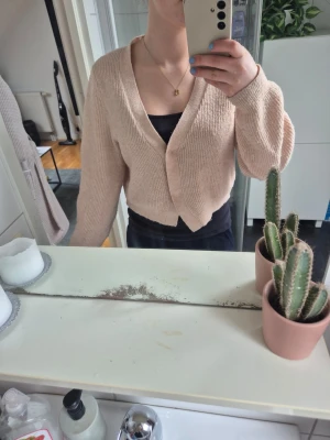 Beige ribbstickad kofta - Säljer en beige ribbstickad kofta med v-ringning och knapp framtill. Koftan är kortare i modellen och har långa ärmar. Perfekt att slänga över en topp för en chill look.