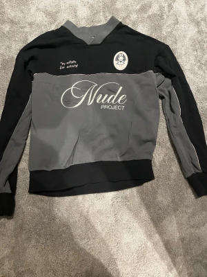 Svart och grå sweatshirt Nude Project - Storlek M. Cool svart och grå sweatshirt från Nude Project med broderad logga och texten 'Nude Project' framtill. Tröjan har rund halsringning, långa ärmar och kontrastpaneler. Materialet känns mjukt och bekvämt, perfekt för en avslappnad streetwear-look. Ordinarie pris 1200
