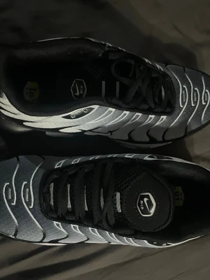 Nike Air Max Tn - Aldrig använda. Nike Air Max tn sneakers i svart och vitt med ikoniska vågformade detaljer och synlig Air-enhet i sulan. Ovandelen är i mesh med svarta och vita kontraster, och skorna har svarta skosnören samt en liten Swoosh på sidan. Perfekta för dig som gillar streetwear och sportig stil.