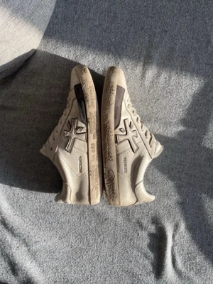 Vita sneakers från Premiata - Snygga beige sneakers från Premiata med grå detaljer och logga på sidan. Skorna har lågt skaft, klassisk snörning och är tillverkade i läder. Perfekta för dig som gillar stilrena och trendiga skor🔥. Originalpåse medföljs och väldigt sparsamt använda! Köpt nya sulor! Skriv till mig om eventuella frågor!☺️