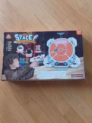 Space Shooting elektroniskt leksaksspel - Space Shooting är ett elektroniskt leksaksspel med en vit och orange måltavla och tillhörande vit laserpistol. Spelet har digital poängräknare och passar för barn från 4 år. Perfekt för att utmana vänner i prickskytte inomhus. Ny i förpackningen. 