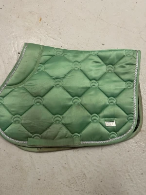 Mintgrönt schabrak från Börjes - Snyggt mintgrönt schabrak från Börjes  med quiltat mönster och silverfärgad kant. Tillverkat i glansigt material som ger en exklusiv känsla. Perfekt till hästutrustningen för dig som vill sticka ut i stallet. Hoppning 