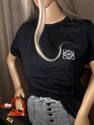 Svart t-shirt från Loewe med logga - Snygg svart t-shirt från Loewe med vit broderad logga på bröstet. Klassisk passform och rund halsringning, perfekt till jeans eller kjol. Tillverkad i mjuk bomull för skön känsla hela dagen.