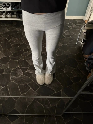 Grå ribbade mjukisbyxor med utsvängda ben - Säljer ett par ljusgrå mjukisbyxor med bred ribbad midja och utsvängda ben. Byxorna är i mjukt och stretchigt material, perfekta för chill dagar hemma. Snygg passform som sitter tajt upptill och släpper nedtill.