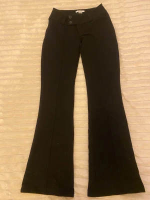 Svarta bootcut kostymbyxor - Snygga svarta kostymbyxor med bootcut-modell och pressveck framtill. Byxorna har hög midja och stängs med två knappar och dragkedja. Perfekta för en stilren och trendig look.
