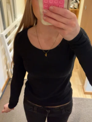 Svart långärmad topp i bomull - En enkel och stilren svart långärmad topp med rund halsringning. Toppen har en slim passform och är tillverkad i mjuk bomull, perfekt att matcha med jeans eller kjol för en clean look.