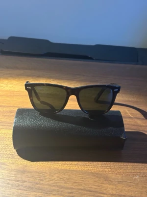 Svarta/orangea Wayfarer solglasögon - Klassiska svarta med lite orangea detaljer Ray-ban Wayfarer med gröna glas och stilren design. Bågarna är i plast och har en tidlös form som passar till de flesta outfits. Perfekta för vår och sommar 💯🏄‍♂️💸☀️(pris kan diskuteras)