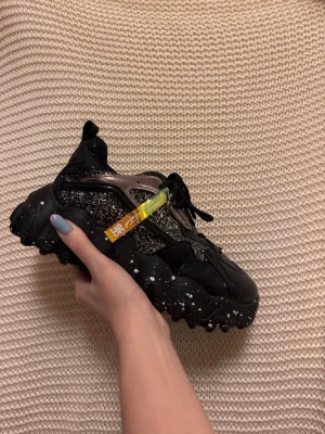 Svarta sneakers  - Säljer ett par svarta sneakers med glittriga metallic-detaljer, skorna är aldrig använda. Storlek 40 men passar som 39. Orginal pris: 660kr