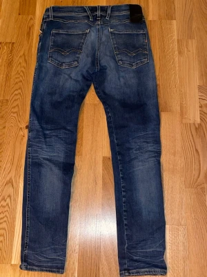 Mörkblå jeans från Replay - Säljer ett par mörkblå jeans från Replay med snygga slitningar och klassisk femficksmodell. Jeansen har raka ben och kontrastsömmar, tillverkade i denim med en skön känsla. Perfekta för dig som gillar en avslappnad men stilren look. Helt klart ett par lite sjystare jeans 