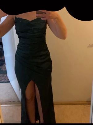 grön klänning med slits - Elegant mörkgrön långklänning med draperad överdel och hög slits framtill. Klänningen har en figurnära passform och är ärmlös, perfekt för speciella tillfällen. Inga skador, använd endast 1 gång. Skriv för fler bilder 