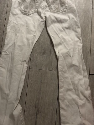 Vita bootcut jeans med broderade fickor - Säljer ett par vita bootcut jeans med snygga broderade detaljer på bakfickorna. Jeansen har normal midja och är tillverkade i ett mjukt bomullsmaterial. Perfekta för dig som vill ha en clean och fräsch look.