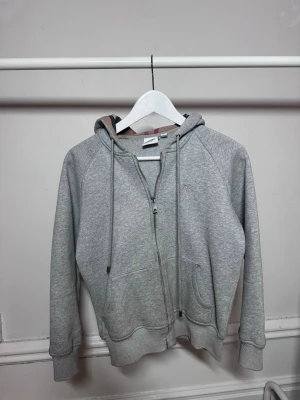 Grå zip hoodie från Burberry -  Snygg grå zip hoodie från Burberry med klassiskt rutigt foder i huvan. Hoodien har dragsko i huvan, två fickor fram och ribbade muddar vid ärmar och nederkant. Perfekt för en avslappnad och trendig look. Hör av dig vid frågor eller funderingar eller vill ha fler bilder🙌