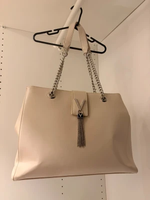 Beige handväska med kedjeremmar - Beige handväska från 💸Valentino 💸med silverfärgade detaljer. 🪩Väskan har flera innerfack där tex dator, böcker får plats. Den är i mycket fint skick! 🤩