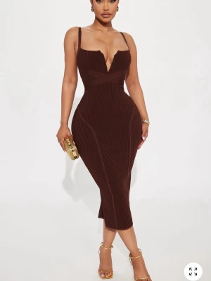 Brun ribbad midiklänning med v-ringning - Snygg brun ribbad klänning med djup v-ringning och smala axelband. Klänningen har en figurnära passform och markerad midja som framhäver siluetten. Perfekt för dig som vill sticka ut med en elegant och trendig look. Helt ny och oanvänd.