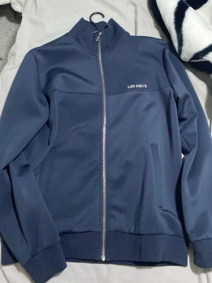 Marinblå ziptröja från Les Deux    Den passar S o M o L - Snygg marinblå ziptröja från Les Deux med hög krage och silverfärgad dragkedja. Tröjan har diskret logga på bröstet och två fickor framtill. Perfekt för en clean och sportig stil.