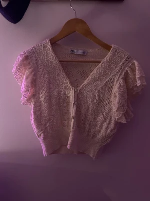 Vit spetskofta från Zara - Kort, vit kofta från Zara med v-ringning och knappar framtill. 