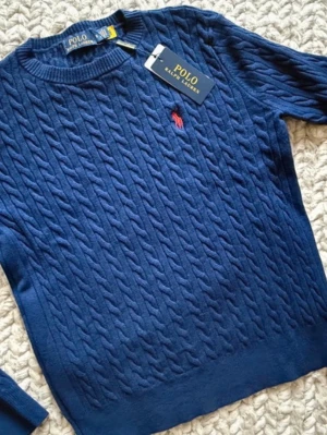 Blå kabelstickad tröja Polo Ralph Lauren - Mörkblå kabelstickad tröja från Polo Ralph Lauren med klassisk röd broderad logga på bröstet. Tröjan har rund halsringning och ribbade muddar. Tillverkad i mjukt material som ger en skön känsla och snygg passform. PRIS KAN DISKUTERAS