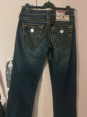 True Religion mörkblå jeans med kontrastsömmar - Säljer ett par mörkblå jeans från True Religion med tydliga kontrastsömnae i orangeat och supersnygga fickdetaljer bak 💓 Jag är 162 och dom passar mig perfekt, storlek S 💓