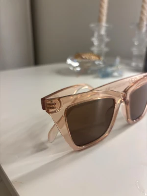 Beige transparenta solglasögon - Snygga solglasögon med transparent beige båge och bruna glas. Ramen har en modern, kantig form som ger en trendig look. Perfekta för dig som vill ha en stilren accessoar till sommaren.
