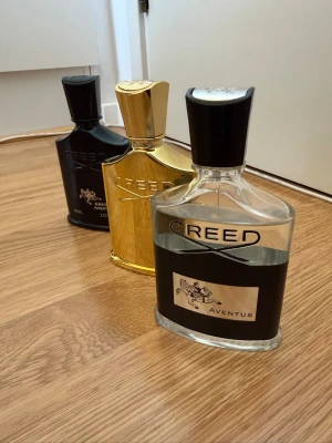 Creed Aventus parfym trio - Säljer tre exklusiva Creed Aventus parfymer i olika utföranden: en klassisk genomskinlig flaska med svart etikett, en helsvart flaska och en lyxig guldfärgad flaska. Alla har elegant design med svarta lock och tydlig Creed-logga. Perfekt för dig som gillar lyxiga dofter.