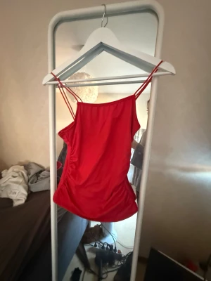 Röd linnetopp med smala axelband - Snygg röd linnetopp med tunna axelband och enkel, stilren design. Perfekt för varma dagar eller att styla lager på lager. Toppens material känns mjukt och följsamt mot huden.