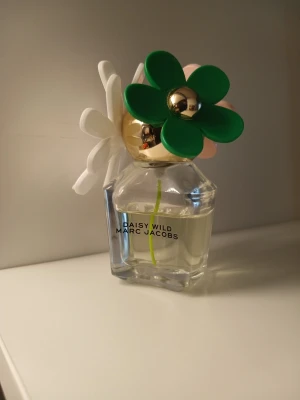 Marc Jacobs Daisy Wild parfym💚🌸 - Säljer en Daisy Wild parfym från Marc Jacobs. Flaskan är genomskinlig med gulddetaljer och har en unik kork dekorerad med stora plastblommor i grönt, vitt och rosa. Parfymen har en modern och lekfull design som sticker ut på hyllan. Väldigt lekfull, flirtig och söt sensuell doft, alldeles perfekt nu till våren💞💞