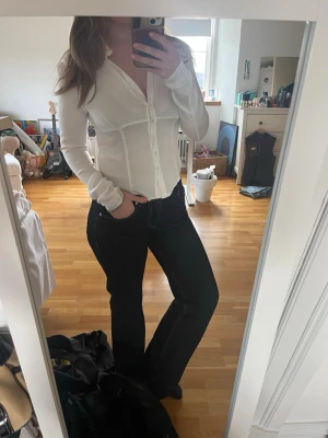 Vit figurnära skjorta med knappar - Säljer en vit, långärmad skjorta med kroppsydd passform och djup v-ringning. Skjortan har knappar framtill och är gjord i ett tunt, stretchigt material som sitter snyggt. Använd en gång men i perfekt form! Säljer pga att jag har för många liknande.