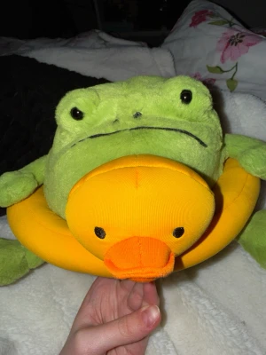 Jellycat Ricky Rain Frog Rubber Ring - Mjukisdjur från Jellycat föreställande en grön groda med en stor gul badanka runt magen. Grodan har svarta broderade ögon och ett glatt uttryck. Badankan är i starkt gul tyg med orange näbb. Perfekt som present eller dekoration. (Helt slutsåld och ”discontinued”, därav görs inte fler av just denna modell, vilket gör värdet mycket högre.) (Samt lappen kvar och gosedjuret i mycket gott skick.)