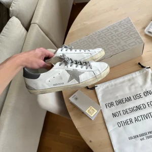 Golden Goose vita sneakers med grå stjärna - Tja! Säljer ett par Golden goose i dunder skick 9/10, Finns såklart lite smuts men inga skador på skorna överlag. Köpta för en månad sedan på Minto (Orderbekräftelse finns). Tillbehör: Box, dustbag, tags. Hör av er vid funderingar!😁